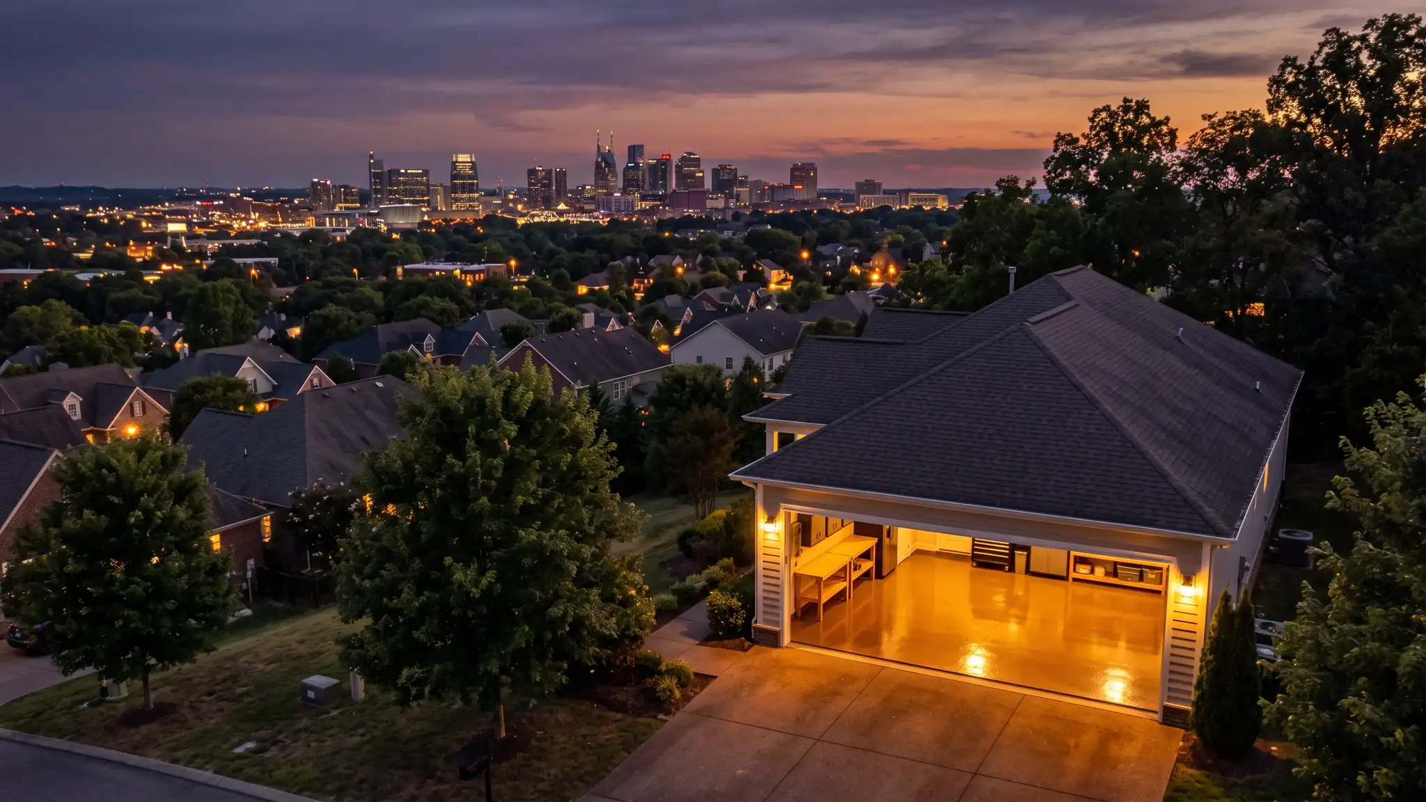 A dramatic dusk view of the Nashville skyline over rooftops and a lit suburban garage with a glossy floor glowing in the foreground